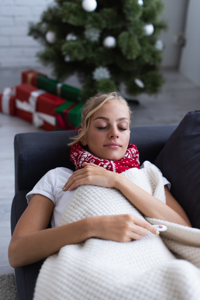sick woman sleeping on sofa near presents and christmas tree on blurred background - Фото, изображение