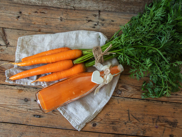 Succo di carota spremuto fresco in una bottiglia di vetro su una superficie di legno. Note di alimentazione, disintossicazione, dieta e concetto vegetariano. - Foto, immagini
