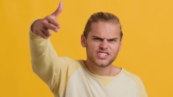 Επιθετικός νεαρός άνδρας γυρίσματα στην κάμερα με το δάχτυλο όπλο πάνω από το κίτρινο φόντο - Πλάνα, βίντεο
