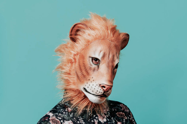 closeup of a young man wearing a lion mask on a blue background with some blank space around him - Photo, Image