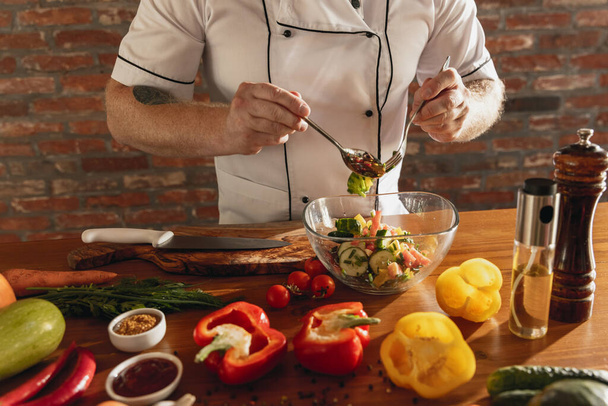 Close-up hands of male chef, cook preparing fresh vegetable salad in his cafe, restaurant kitchen. Concept of a correct, healthy diet. - Фото, изображение