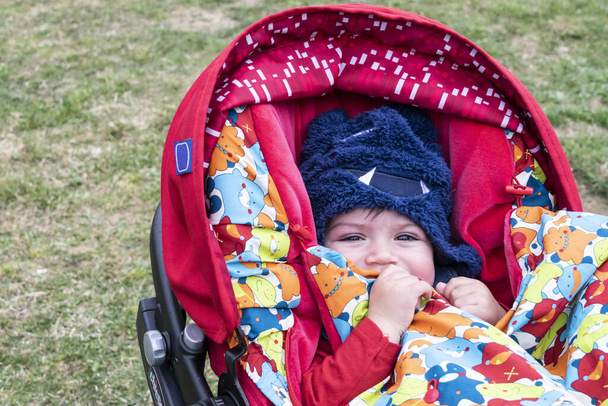Маленький хлопчик в колясці вкритий від холоду капелюхом і ковдрою. Привіт про несподівану холодну погоду через зміну клімату
 - Фото, зображення