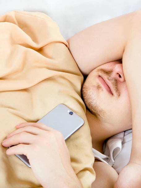 Junger Mann schläft mit Handy in Großaufnahme im Bett - Foto, Bild