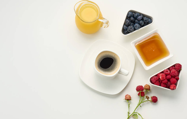 freshly squeezed juice in a glass transparent decanter, a cup of coffee, honey and oatmeal on a white table. Morning breakfast, top view - Foto, immagini