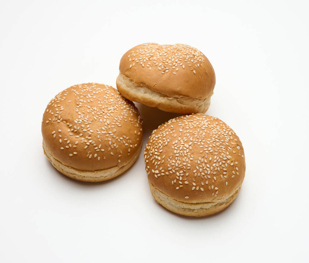 gebakken rond verse witte tarwebloem, bestrooid met sesamzaad op een witte tafel. Hamburger, cheeseberger en broodjesbroodje - Foto, afbeelding