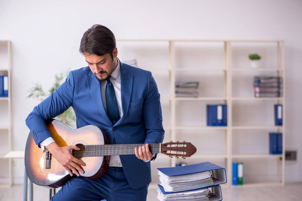 Young male employee playing guitar at workplace - Zdjęcie, obraz