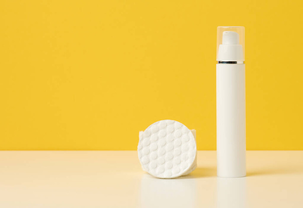cosmetic products in a white plastic bottle and white cotton pad. Blank for branding products, moisturizer on yellow background - Photo, Image
