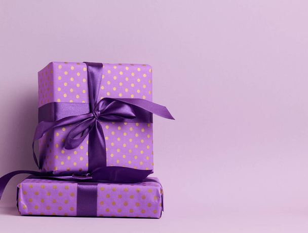 boxes packed in festive purple paper and tied with silk ribbon on a purple background, birthday gift, surprise - Photo, Image