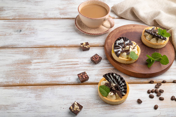 Sweet tartlets with chocolate and cheese cream with cup of coffee on a white wooden background and linen textile. side view, copy space. - Foto, Bild