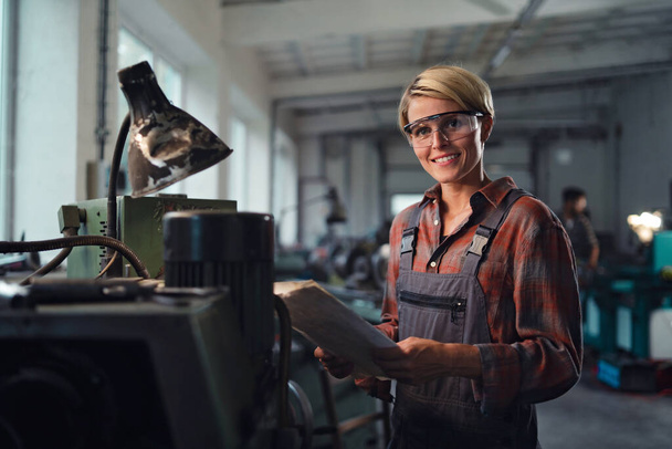 Portrait of mid adult industrial woman working indoors in metal workshop, looking at camera. - Foto, Imagen