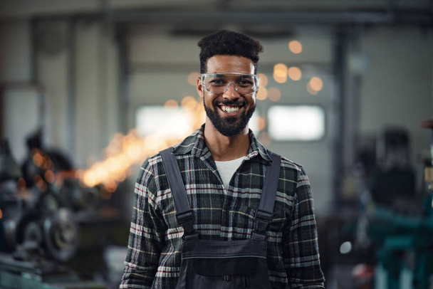 Portrait of young industrial man working indoors in metal workshop, looking at camera. - Fotó, kép
