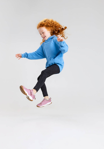 Retrato de niña caucásica, niño posando en movimiento aislado sobre fondo gris estudio. - Foto, Imagen