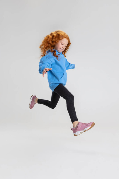 Retrato de niña caucásica, niño saltando y posando aislado sobre fondo gris estudio. - Foto, Imagen