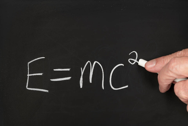A teacher writes the theory of relativity Einstein equation on a black chalkboard while teaching a group of students in a classroom - Foto, Imagem