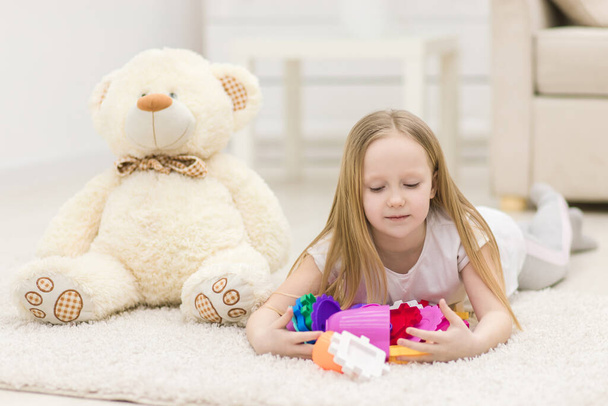 Photo of blond girl looking at the camera laying on the floor with toys. - Photo, image