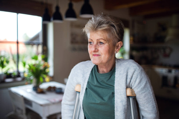 Portrait of senior woman with crutches indoors at home, looking aside. - Foto, imagen