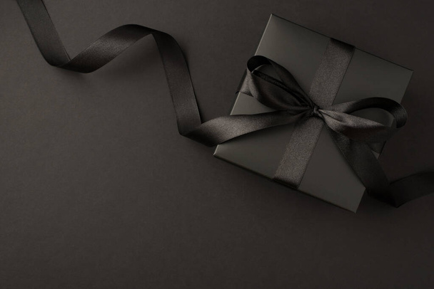 Foto vista superior de caja de regalo negra con lazo de cinta negra sobre fondo negro aislado con espacio vacío - Foto, Imagen