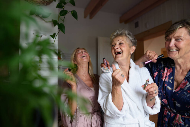 Happy senior women friends in bathrobes having fun indoors at home, selfcare concept. - Фото, зображення