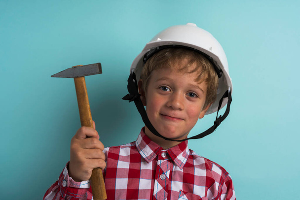 A cute boy in a construction helmet with a hammer in his hand, A portrait of a small builder in a helmet. - Fotografie, Obrázek