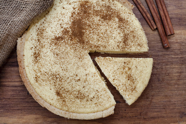 Traditional South African milk tart on rustic wooden table, sprinkled with cinnamon and styled with cinnamon coils - Foto, immagini