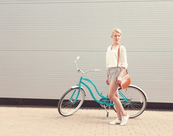 Beautiful blonde girl is standing near the vintage bicycle with brown vintage bag, warm, tonning - Foto, imagen
