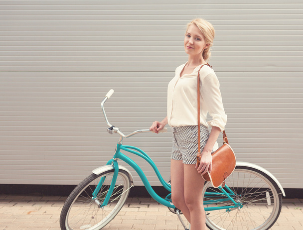 Beautiful blonde girl is standing near the vintage bicycle with brown vintage bag have fun and good mood looking in camera and smiling, warm, tonning - Fotoğraf, Görsel
