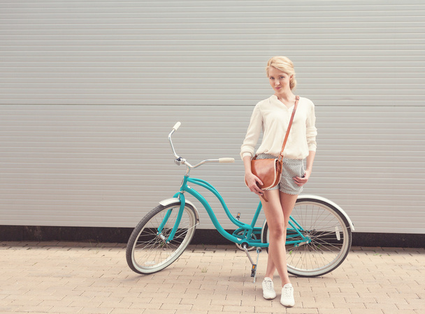 Beautiful blonde girl is standing near the vintage bicycle with brown vintage bag have fun and good mood looking in camera and smiling, warm, tonning - Foto, immagini