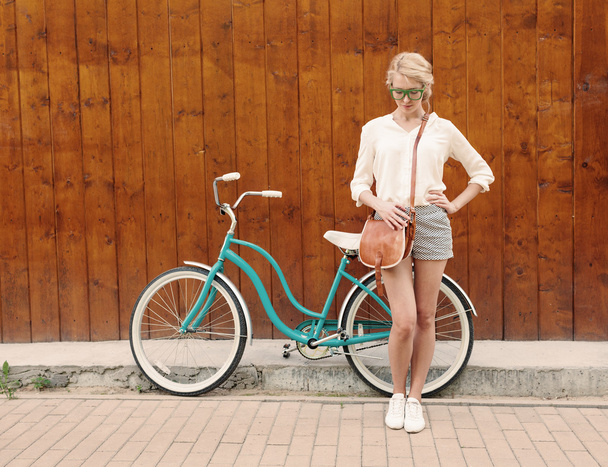 Young sexy blonde girl is standing near the vintage green bicycle with brown vintage bag in green sunglasses, warm, tonning - 写真・画像