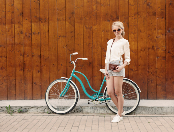 Young sexy blonde girl is standing near the vintage green bicycle with brown vintage Cameras in orange sunglasses., warm, tonning - Fotografie, Obrázek