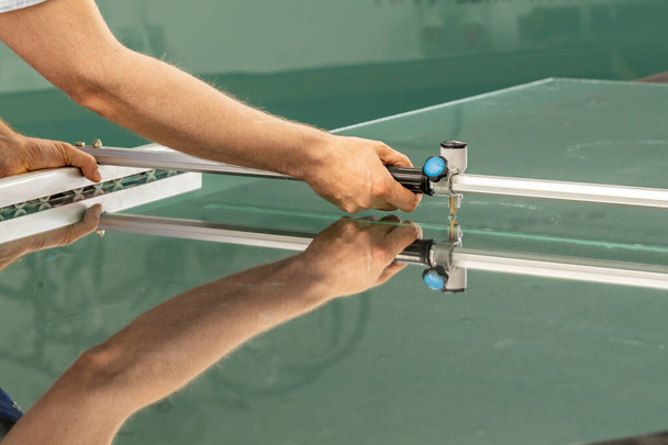 Сотрудник стекольной фабрики режет стекло специализированным оборудованием  - Фото, изображение