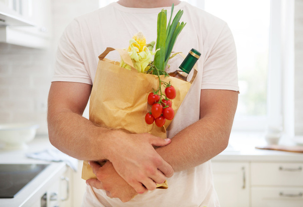 człowiek posiadający papierową torbę pełną artykułów spożywczych w kuchni  - Zdjęcie, obraz