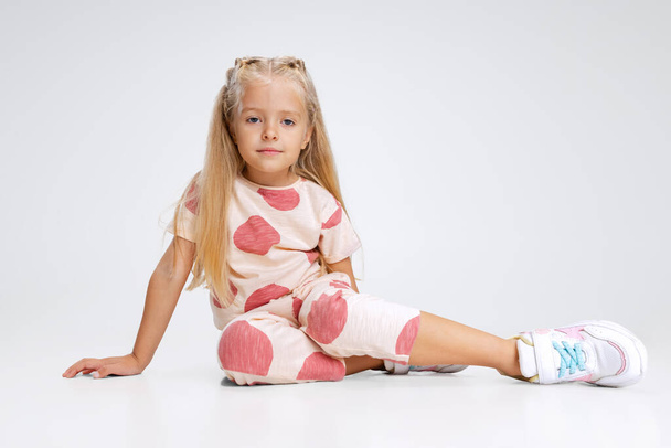 Full-length portrait of little Caucasian girl, child posing isolated over white studio background. Calmly sitting - Foto, afbeelding