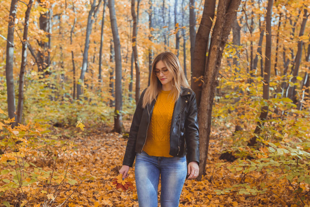 Chica sostiene hojas caídas y camina en el parque de otoño. Concepto estacional. - Foto, Imagen