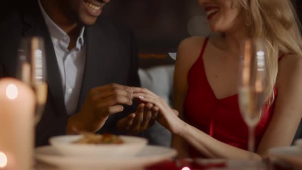 Черный мужчина делает предложение женщине, надевая кольцо в ресторане - Кадры, видео