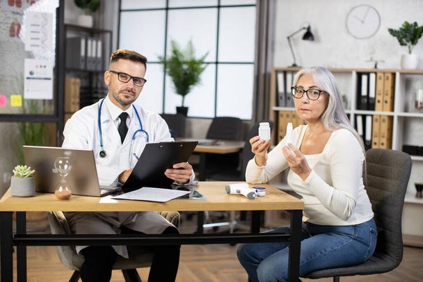 Doctor and patient looking at camera while sitting at office - Photo, image