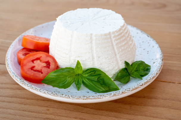 Colección de quesos, ricotta italiana blanca de queso blando servida con tomates frescos y albahaca servida al aire libre con casas italianas sobre fondo - Foto, imagen