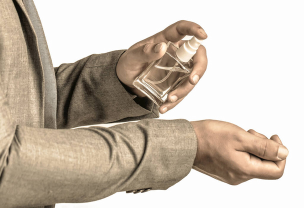 Fashion cologne bottle. Fragrance smell. Men perfumes. Handsome man in formal suit and with bottle of perfume, closeup. Man holding up bottle of perfume. Men perfume in the hand on suit background - Photo, Image