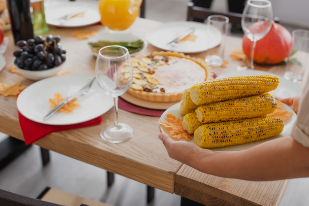 Cropped view of african american woman holding baked corn near thanksgiving dinner  - Foto, Imagen