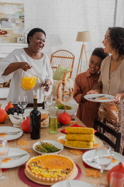 Улыбающаяся африканская американская семья с ребенком, подающим ужин в честь Дня благодарения  - Фото, изображение