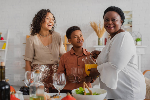 Afroamerikanerin lächelt während eines Dankeschön-Abendessens neben Tochter und Enkel in die Kamera  - Foto, Bild