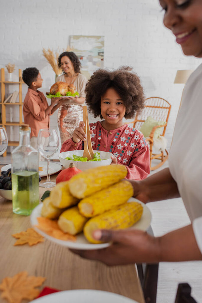Cheerful african american kid holding salad near blurred granny and thanksgiving dinner  - Фото, зображення