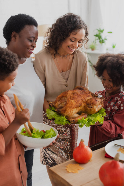 Cheerful african american woman holding traditional turkey near family at home  - Foto, immagini
