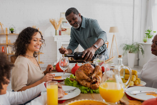 African american man pouring wine near family and thanksgiving dinner  - Foto, Bild