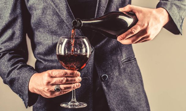 Červené víno se nalévá z láhve do skla. Láhev s gurmánským nápojem, sklenice s červeným vínem, sommelier, ochutnávka. Číšník nalévá červené víno do sklenice. Sommelier muž, degustace, vinařství, muž vinař - Fotografie, Obrázek