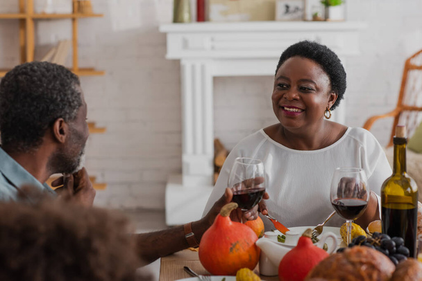 Donna afroamericana matura che guarda il marito con il vino durante la cena del Ringraziamento  - Foto, immagini