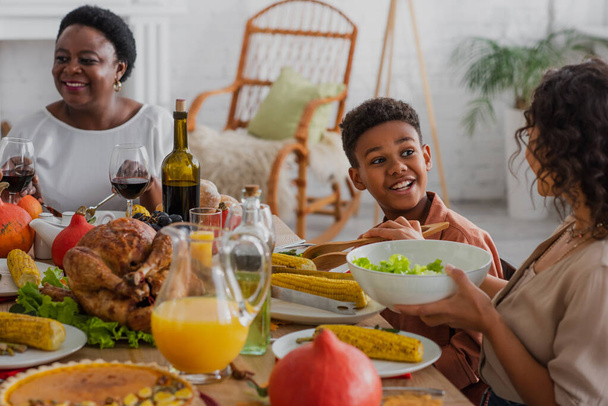Sonriente niño afroamericano mirando a la madre cerca de deliciosa cena de acción de gracias  - Foto, Imagen