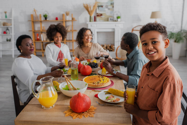 Smiling african american boy holding orange juice near family at thanksgiving dinner  - Photo, Image