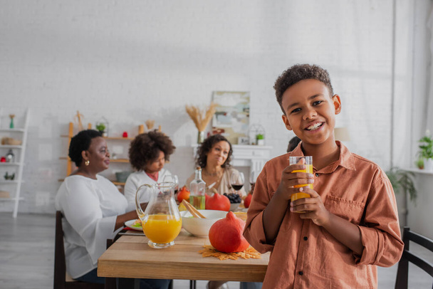 African american boy holding orange juice near blurred family during thanksgiving  - Photo, Image