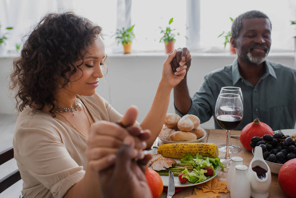 african american woman holding hands with parents while praying before thanksgiving dinner with closed eyes - Photo, Image