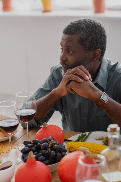 Африканский мужчина среднего возраста, сидящий с сжатыми руками за столом за праздничным ужином - Фото, изображение